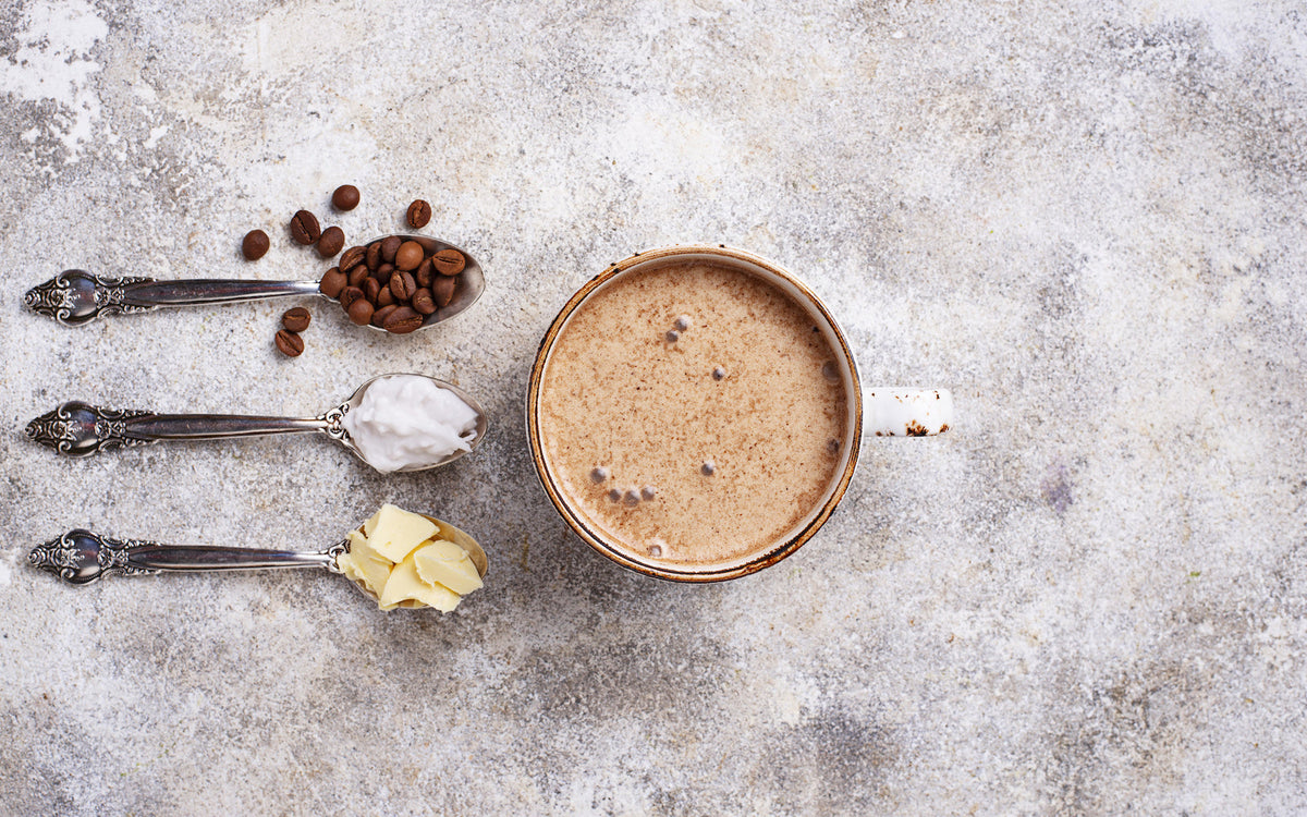 Bulletproof coffee UK: Person holding a glass cup with coffee on a wooden board 
