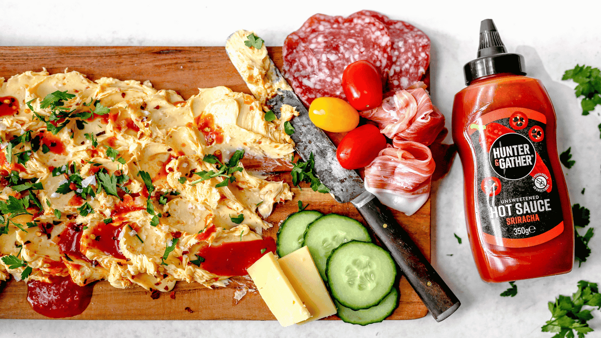 chopping board with spicy butter, meats, tomato, cucumber, butter and hunter gather sriracha hot sauce