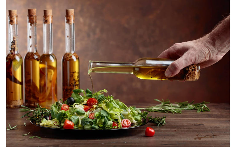 hand pouring oil on colorful green salad with bottles of cooking oil in background.