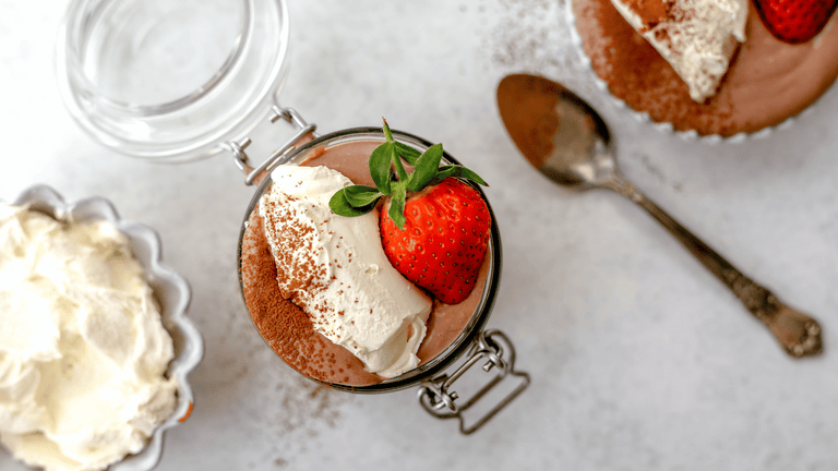 chocolate mousse in a glass jar with whipped cream and a strawberry and spoon