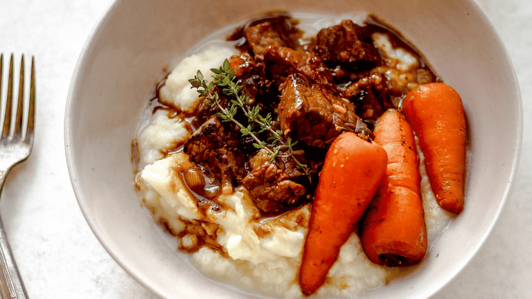 braised beef with carrots and cauliflower mash in a bowl on a table