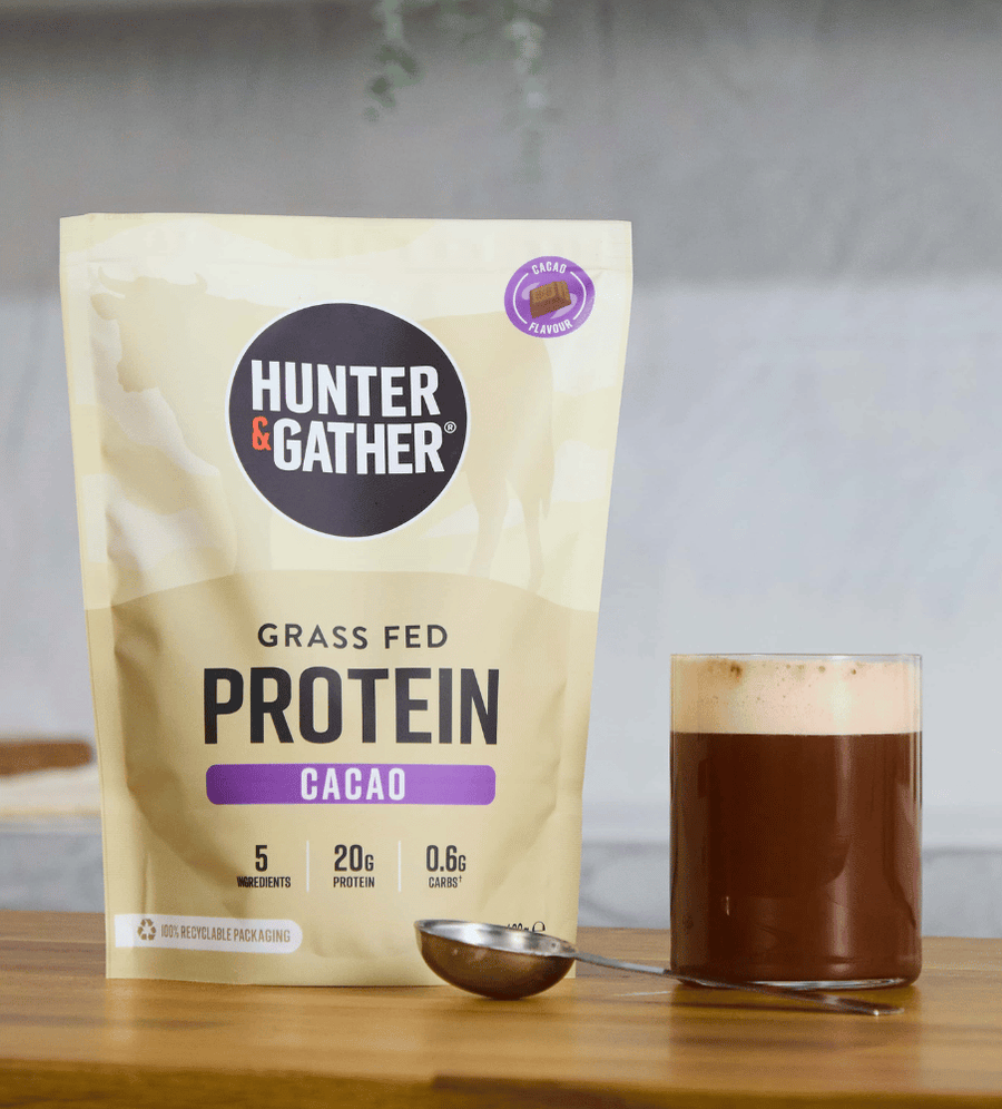 Hunter & Gather grass fed protein cacao package with a glass of chocolate shake on a wooden surface.