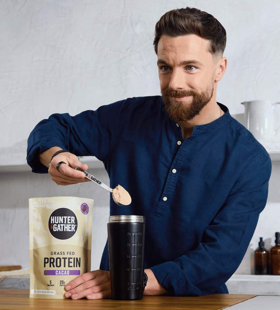 Man pouring Hunter Gather protein powder into a shaker bottle with a white background