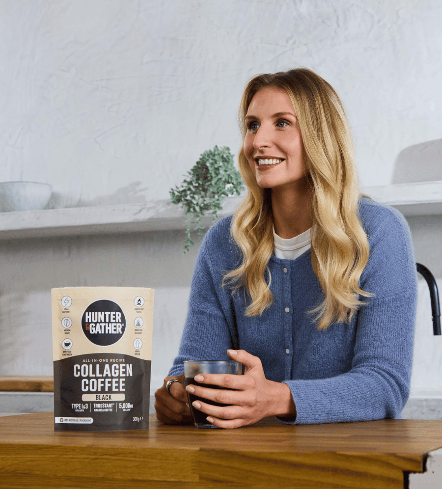 Woman holding a glass of collagen coffee with a package of Hunter and Gather Collagen Coffee on a table.
