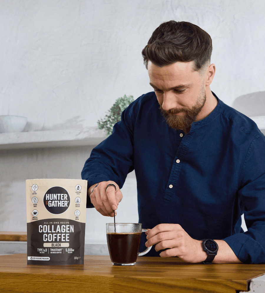 Man stirring a cup of coffee with a Hunter Gather collagen coffee package on a table.