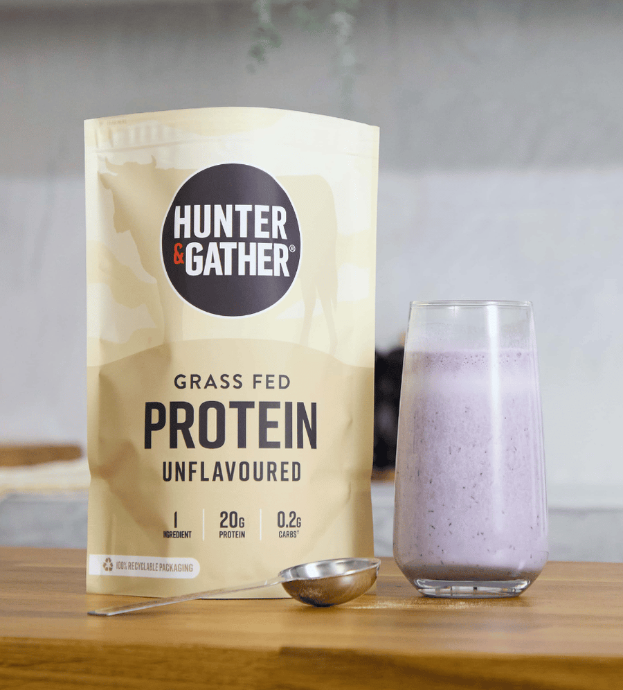 Hunter & Gather grass fed protein package with a glass of purple shake on a wooden surface.